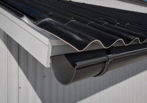 Schwarzes Dachblech mit gebogenem Profil, das über eine Traufe in eine Dachrinne hineinragt